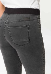 Schwarze, dehnbare Jeans mit einem breiten elastischen Bündchen, Gesäßtaschen und einem Slim-Fit-Design mit dezenten Verblassungen und Nähedetails.