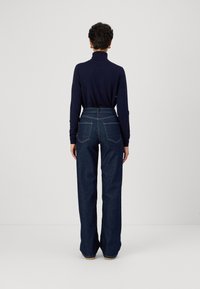 Top a collo collo blu abbinato a jeans in denim scuro a vita alta e gamba larga. I jeans presentano tasche posteriori e dettagli di cucitura discreti.
