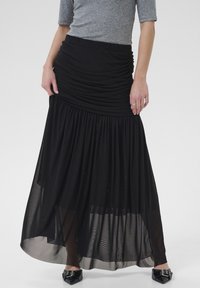 Zwarte maxi-rok van gelaagd materiaal; heeft een gerimpelde taille en een doorschijnende onderkant, met een vloeiende silhouet en subtiele textuur.