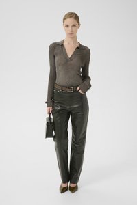 Top lung cu mânecă lungă, metallic de culoare marron, cu guler, asortați cu pantaloni din piele de culoare verde închis. Modelul ține o geantă mică neagră. Curea marron și pantofi ascuțiți.