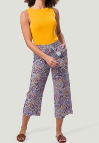 Haut jaune sans manches, pantalon court à motifs violets et jaunes avec cordon de serrage, porté avec des sandales marron à enfiler.