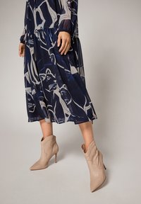 Langärmliges, transparenter Kleid in Marineblau mit Tiermuster und leichtem Stoff. Beigefarbene Knöchelstiefel mit spitzem Fuß und geschwungenem Design.