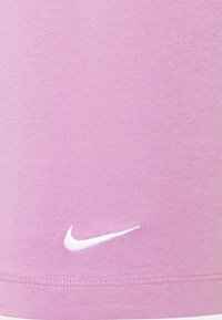 Vaaleanpunainen urheilutoppi, jossa on ribbitekstuuri. Alareunassa valkoinen Nike-logo. Valmistettu joustavasta ja hengittävästä kankaasta.