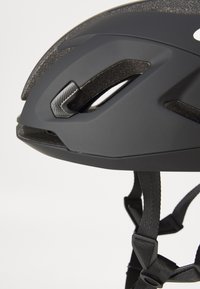 Schwarzer Fahrradhelm mit matter Oberfläche, aerodynamischer Form, mehreren Belüftungsöffnungen, strukturierten Akzenten und verstellbaren schwarzen Riemen.