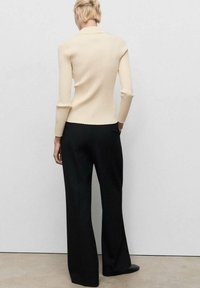 Top a maniche lunghe beige a coste abbinato a pantaloni neri a gamba larga. Tessuto in misto cotone, design aderente e texture liscia.