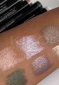 Ihoon levitettyjä hohtavia luomivärinäytteitä: ruusukulta, laventeli, oliivinvihreä ja pronssi. Taustalla mustia kynärajauksia.