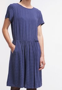 Marinblå klänning med vita prickar, korta ärmar, elastisk midja och sidofickor. Slät tyg med en avslappnad, flödande form.