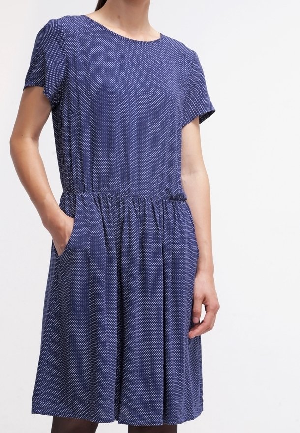 Marinblå klänning med vita prickar, korta ärmar, elastisk midja och sidofickor. Slät tyg med en avslappnad, flödande form.