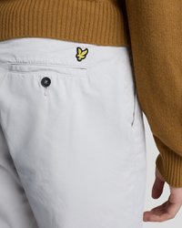 Nahaufnahme von weißen Hosen mit einem schwarzen Knopf und einem gelben Vogel-Logo in der Nähe der Gesäßtasche, getragen mit einem braunen, gerippten Pullover.