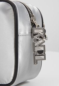 Silbernes Satin-Kosmetiktäschchen mit schwarzem Rand, ausgestattet mit einem silbernen Reißverschluss und einem auffälligen schwarz-weißen Logoschild mit der Aufschrift "KARL."