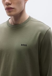 Λαδί μακρυμάνικο πουκάμισο με στρογγυλή λαιμόκοψη. Διαθέτει μαύρο λογότυ�πο "BOSS" στην αριστερή περιοχή του στήθους. Ομαλή υφή και εφαρμοστή γραμμή.