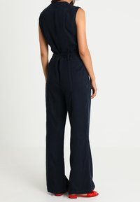 Námořnická modrá kombinéza bez rukávů, s opaskem v pase a širokým nohavicovým střihem. Hladká textura s minimem švů.