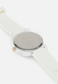 Orologio con cinturino in silicone bianco e fondello in acciaio inox argento rotondo. Logo inciso, particolare dorato sulla corona. Texture liscia, design minimalista.