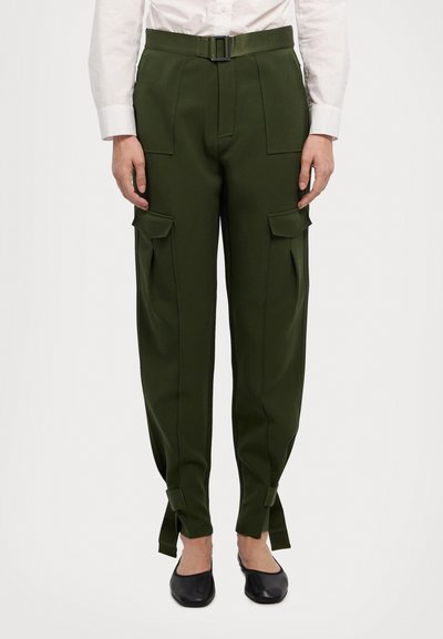 Grüne Cargo-Hosen mit einem Gürtel, die mehrere Taschen, schmal zulaufende Beine und Krawatten am Saum haben. Kombiniert mit einem weißen Hemd mit Kragen und schwarzen Ballerinas.