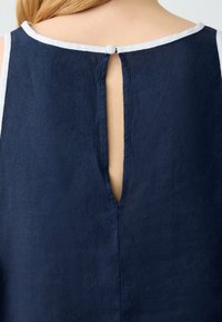 Top in lino blu navy con scollatura rotonda e apertura a chiave sul retro fissata da un bottone. Presenta un profilo bianco lungo il collo.