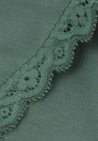 Groene stof met ingewikkelde kantafwerking met geschulpte randen en kleine bloemenuitsparingen. Soepele textuur met gedetailleerde patronen langs de rand.