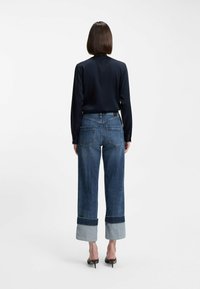 Marinblå blus med långa ärmar kombinerad med högmidjade, vida jeans med uppvikta fållar. Mjukt tyg, klassisk design, strukturerad passform.