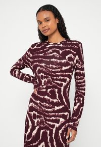 Haljina s dugim rukavima u tamno bordo boji s bijelim apstraktnim uzorkom. Glatka, rastezljiva tkanina, pripijeni kroj i okrugli izrez oko vrata.