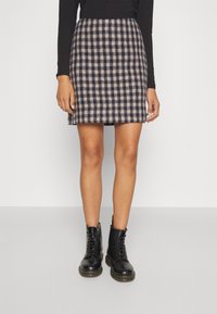 Falda de lana a cuadros en azul marino y beige, con silueta en A, combinada con botas negras de cordones con acentos amarillos y una textura suave.