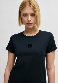 Czarna bawełniana koszulka z krótkim rękawem, z teksturowanym, haftowanym logo na piersi. Gładki materiał i standardowy krój.