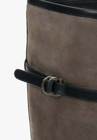 Hnědá semišová taška s černými koženými akcenty, disponující tenkým koženým popruhem zajištěným stříbrnou sponou, hladkým povrchem a válcovým tvarem.