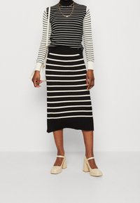 Gestreiftes, schwarzes und weißes, geripptes Sweater- und Midirock-Set, das ein figurbetontes Design und einen strukturierten Stoff aufweist, kombiniert mit cremefarbenen, klobigen Absatzschuhen.