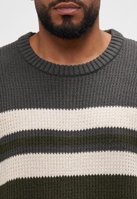 Strickpullover in Dunkelgrün und Creme, mit horizontalen Streifen. Gerippter Rundhalsausschnitt und strukturierter Stoff.