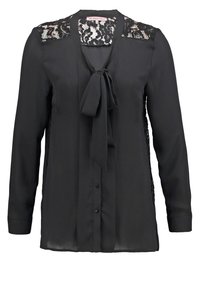 Blusa nera a maniche lunghe, con dettagli in pizzo sulle spalle, scollatura annodata, chiusura a bottoni e pannelli laterali trasparenti. Tessuto liscio con una texture morbida.