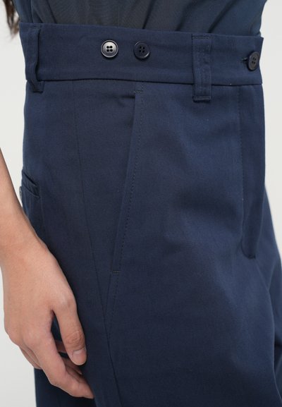 Pantaloni bleu marin dintr-un material neted, cu două butoane negre și o buzunar lateral. Talia este croit cu o cusătură elegantă.