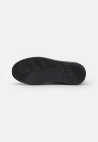 Black rubber shoe sole featuring a textured grip pattern and a circular logo. The design includes a flat, slightly raised edge.