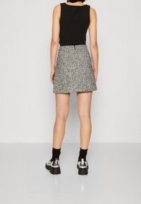 Žena stojící zády, oblečená v černém bezrukávovém topu, sukni s černo-bílým vzorem, černých ponožkách a stříbrných masivních botách.