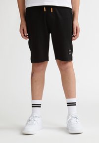 Pantalones cortos negros con cintura elástica y cordones naranjas, con un logo en la pierna izquierda. Combinados con zapatillas blancas y calcetines a rayas.