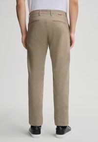 Pantaloni beige in tessuto intrecciato con taglio dritto, tasche standard e una texture sottile, abbinati a sneakers nere.