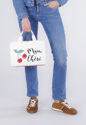 Persona que lleva vaqueros azules, zapatillas marrones y chaqueta vaquera, sosteniendo un bolso blanco con un gráfico de cereza y el texto "Mon Chéri".