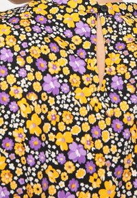 Svart tygblus med ett blommönster i gult och lila. Inkluderar en liten nyckelhålsöppning i ryggen med en knappstängning.