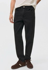 Jeans de denim negro con ajuste recto, dise�ño de cinco bolsillos, cierre de botón en la parte superior y detalles de costura sutiles. Combinados con zapatillas marrones.