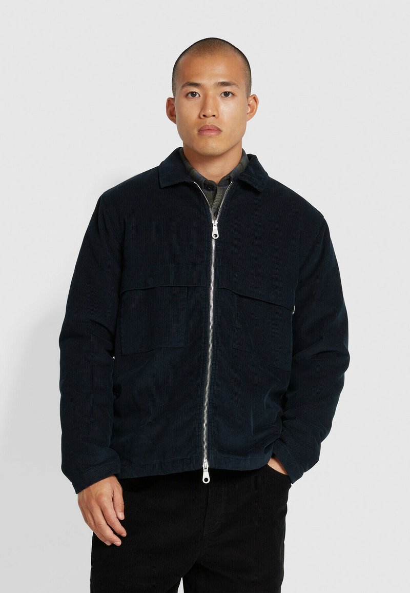 Veste en velours côtelé bleu marine avec fermeture éclair à l'avant, deux poches poitrine et un col. Présente une finition texturée et une coupe décontractée.