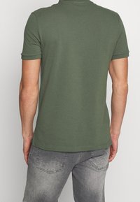 Polo vert à manches courtes en coton, avec une coupe classique, une texture lisse et des poignets côtelés. Vue arrière montrant un design minimaliste.