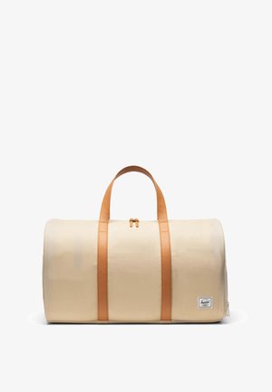 Béžová taška typu duffel s hnedými koženými rukoväťami a vertikálnymi pásmi, horné zapínanie na zips a malá nášivka s logom na dolnej pravej strane.