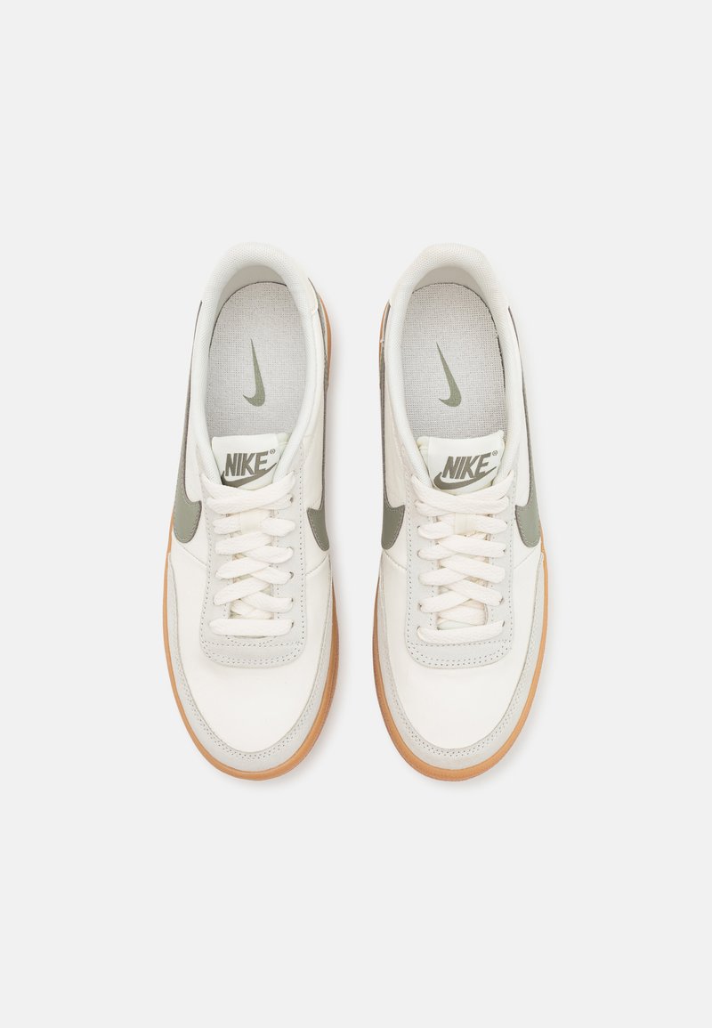 Zapatillas blancas con parte superior de cuero texturizado, acentos verdes y suela de goma. Presentan cordones planos y una etiqueta de marca en la lengüeta.