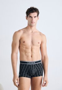 Boxers noirs avec un motif géométrique, arborant un logo Lacoste blanc sur la ceinture, fabriqués en tissu doux et extensible.