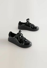 Schwarze Lackledersneaker mit dicker Gummisohle, runder Zehenform und übergroßen Schnürsenkeln. Glatte Textur mit kontrastierenden matten Akzenten.