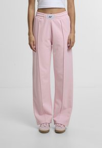 Lyserøde sweatpants med bred benpasform, elastisk talje med et mærke og blød tekstur. Ingen yderligere mønstre eller detaljer til stede.