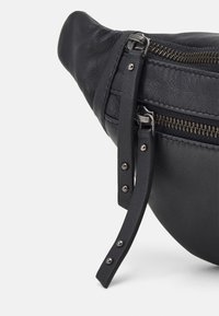 Borsa in pelle nera con superficie testurizzata, dotata di una tasca con zip e di una tracolla con hardware e rivetti in argento. Forma curva con una finitura morbida.