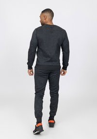 Sweatshirt noir en maille et joggeurs assortis avec un motif texturé, des poignets et une taille côtelés. Chaussures sportives avec des accents orange.