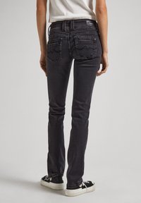 Mustad denim teksad, millel on kitsas lõige, tagaküljel on lainelised õmblusmustrit sisaldavad taskud ning keskmise kõrgusega vöökoht.