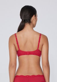 Červená krajková podprsenka s nastavovacími ramínky a květinovým vzorem, vybavená zapínáním na háček a očko. Hladký povrch, minimalistický design.