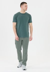 Donker groen gemêleerd T-shirt met korte mouwen en een ronde hals, gecombineerd met lichtgroene sportbroek en grijze hardloopschoenen.
