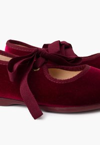 Zapatos de ballet de terciopelo burdeos con punta redondeada, cintas de tela para el cierre y un interior suave. Presentan un brillo sutil y una textura suave.
