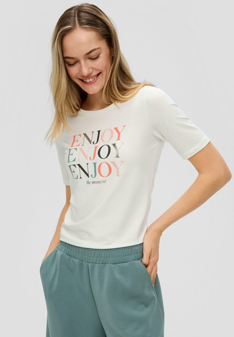 Witte korte mouwen t-shirt met kleurrijke "ENJOY" tekst in verschillende lettertypes, gecombineerd met lichtgroene joggerbroeken met elastische tailleband.